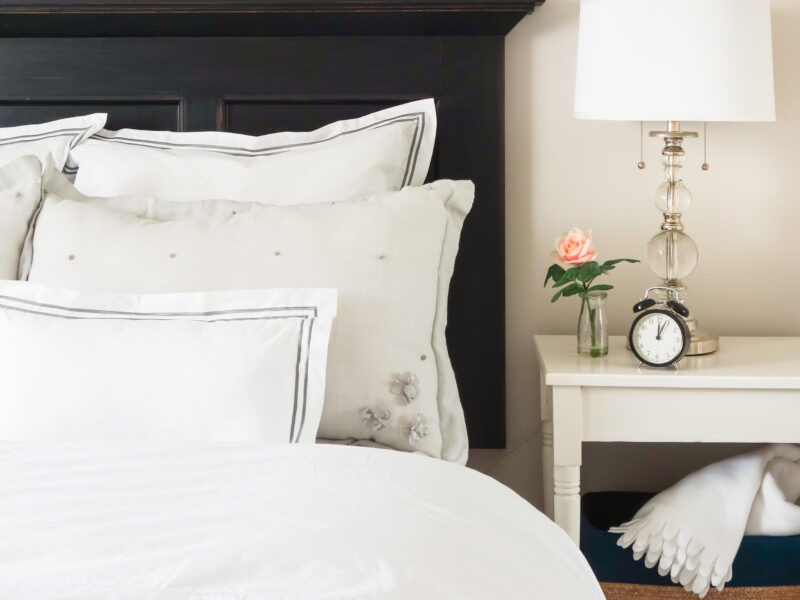 Lake house bedroom, graphic-edge sheets and pillows, crisp white bed linens, vintage night table, black headboard adds contrast to shades of white, Maxine Whitehead design