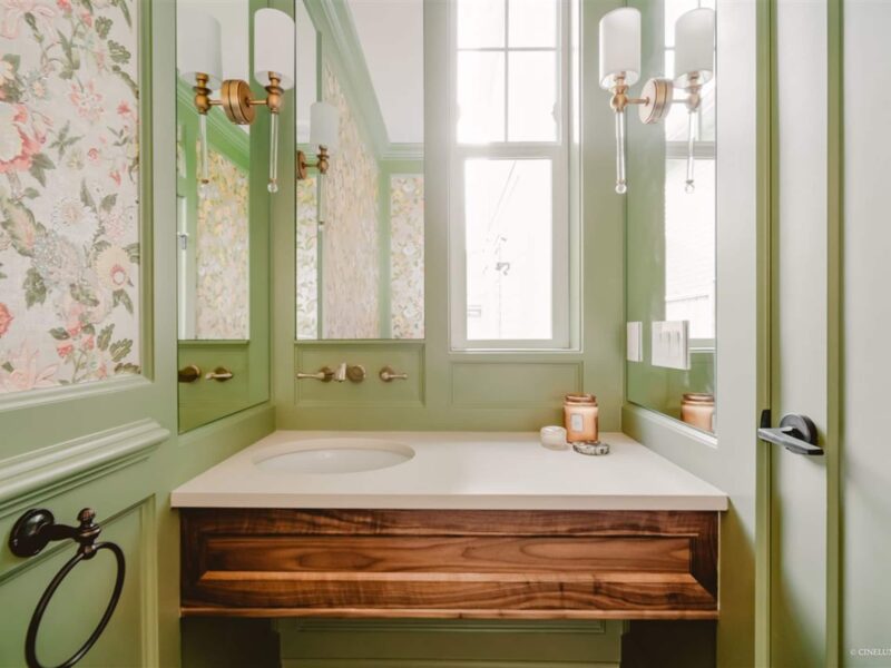 dramatic powder room in vibrant green, elegant wall sconces sparkle in stylish mirrors, champagne brass wall faucet in vintage style, lush wallpaper adds a gorgeous floral element, Maxine Whitehead design